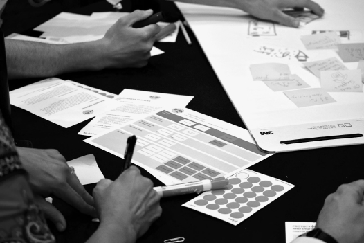 a closeup photo of people's hands during a brainstorming session wit sticky notes, pens, and paper